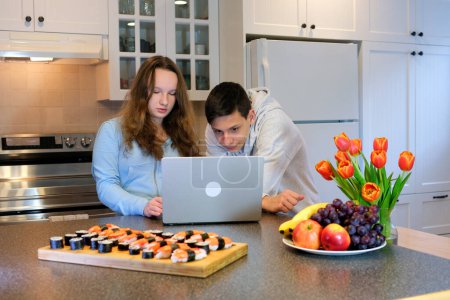 Photo for Choose movie show set up laptop repair teenagers prepared to watch video sushi on table tulips and fruits in kitchen celebrate valentines day birthday invite girl to visit movie attentively - Royalty Free Image