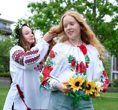 Foto de Hermosas mujeres jóvenes niñas tejiendo guirnaldas caminando riendo charlando en el parque en el jardín bordado camisas nacionales ucranianas guirnaldas de flores de girasol y flores blancas del bosque hermoso vyshyvanka - Imagen libre de derechos