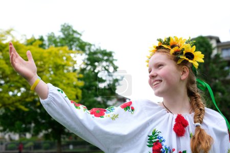 Téléchargez les photos : Jeune fille aux cheveux roux dans une couronne de tournesols à l'extérieur dans le jardin du parc en belle chemise ukrainienne brodée vyshyvanka avec tresse rouge avec rubans Ukraine Temps paisible de joie et de paix - en image libre de droit