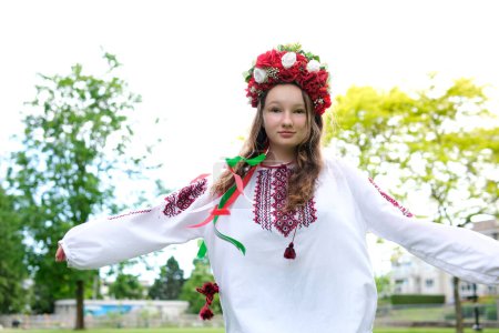 Téléchargez les photos : Belle jeune femme ukrainienne tendre fille en grande couronne rouge de rose vif fleurs rouges blanches filant lissage cheveux tressage rubans dans ses cheveux vent tendresse propreté paix en Ukraine - en image libre de droit