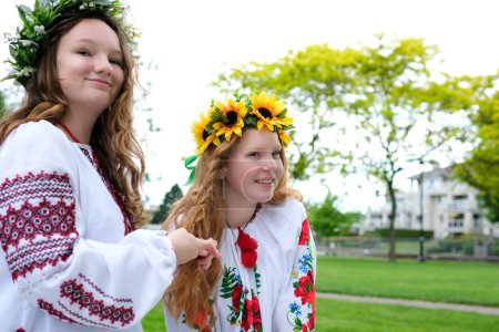 Téléchargez les photos : Belles jeunes femmes filles tisser des couronnes de marche riant bavarder dans le parc dans le jardin brodé national ukrainien chemises couronnes de fleurs de tournesol et de fleurs blanches de la forêt belle vyshyvanka - en image libre de droit