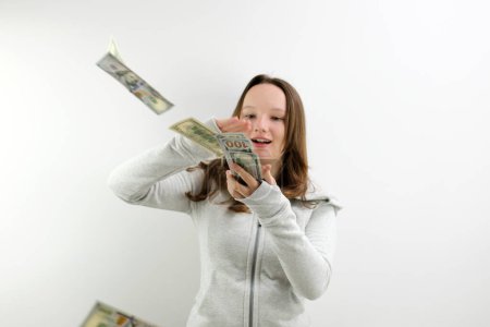 Arrogant wealthy girl scattering dollars with proud haughty expression, boasting rich life, throwing around cash, squandering wasting money carelessly. indoor studio shot isolated