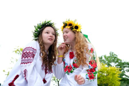 Foto de En pleno verano. Dos chicas en la ropa eslava tejen trenzas en el pelo cerca del fuego. - Imagen libre de derechos