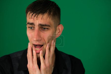 Photo for Emotions of a handsome man guy on a green background chromakey close-up dark hair young man nice man in a black shirt with the beard poses funny faces. High quality photo - Royalty Free Image