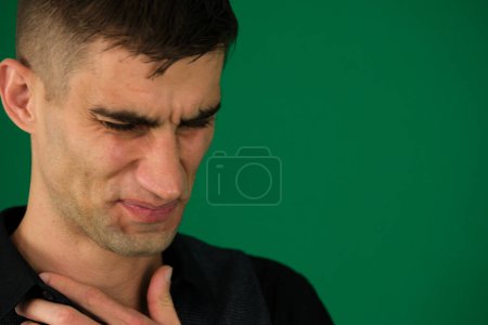 Close-up portrait of a funny crying man emotions of a handsome man guy on a green background chromakey close-up dark hair young man. Men are showing chest pain.