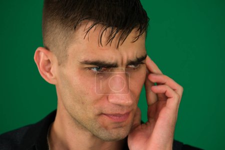 emotions of a handsome man guy on a green background chromakey close-up dark hair young man. good looking dark haired man is looking directly at viewer with a tough expression on his face