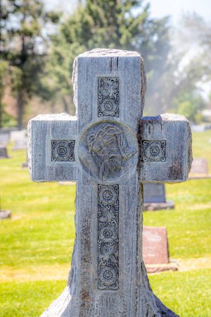 Téléchargez les photos : Une grande pierre tombale en forme de croix religieuse avec le visage de Jésus-Christ à l'intersection d'un cimetière - en image libre de droit