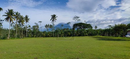 Photo for A soccer field in the Gunung Kawi valley, Malang, East Java with goalposts and plants along the sides. Coconut trees, palm trees, sengon trees, beautiful view - Royalty Free Image