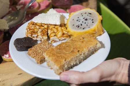 Foto de Plato de comida con: Pastel, turrón de sésamo, pitaya, queso y cacahuetes con caramelo. - Imagen libre de derechos