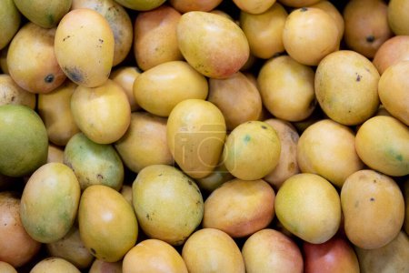 Téléchargez les photos : Fond avec des mangues jaunes et mûres sur le marché. Doux et délicieux. - en image libre de droit