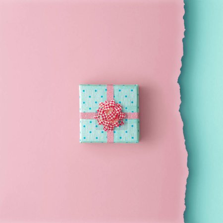 Téléchargez les photos : Composition minimaliste de Noël composée d'une petite boîte cadeau enveloppée d'un ruban rose sur un fond bleu rose. Fond de Noël. Concept minimal. Pose plate. D'en haut. Espace pour écrire - en image libre de droit