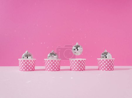 Photo for Disco ball in a paper cup with abstract cupcake flying one against a pastel pink background. Creative New Year or Xmas celebration party concept. Festive food idea. Creative art minimal aesthetics. - Royalty Free Image