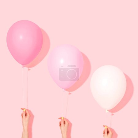 Téléchargez les photos : Ballons rose pastel et blancs avec des mains féminines. style minimal ballons de couleur rose flottant hors du sol sur fond rose. Nature morte surréaliste moderne - en image libre de droit