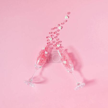 Foto de Composición creativa hecha de dos copas de champán con piedras de cristal rosa y corazones de perlas blancas sobre fondo rosa. Concepto mínimo de San Valentín o amor. Vista superior, espacio de copia. - Imagen libre de derechos
