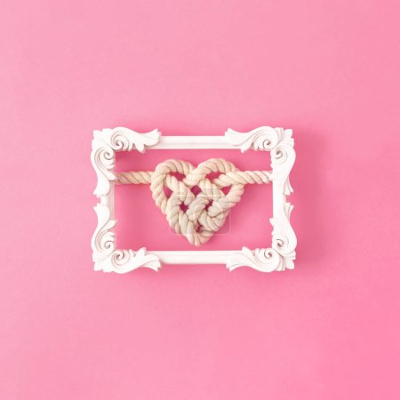 Foto de Cuerda en forma de corazón nudo en un marco de imagen clásico blanco sobre fondo rosa - Imagen libre de derechos