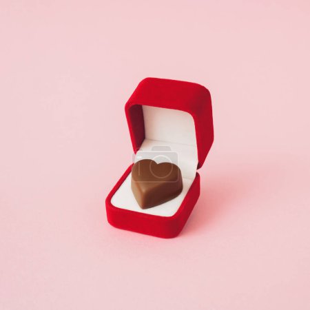 Foto de Composición de amor hecha de caja de anillo de compromiso rojo con corazón de bombones en ella, sobre fondo pastel rosa. Concepto mínimo de San Valentín o amor. Arte creativo, estética mínima. - Imagen libre de derechos