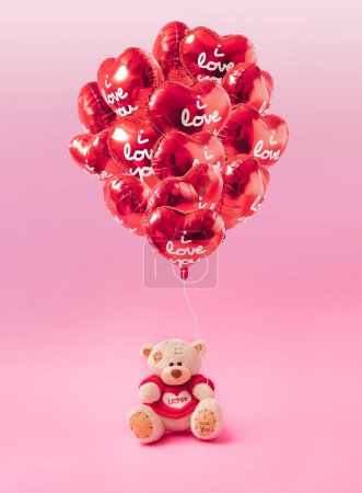 Photo for Love composition made of teddy bear and Bunch of red color heart shaped foil balloons on pastel pink background. Minimal concept of Valentine's Day or love. Creative art, minimal aesthetics. - Royalty Free Image