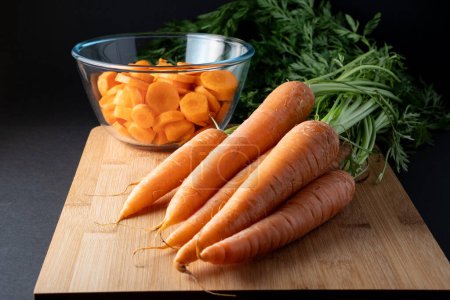tranches de carottes dans un bol en verre rond et des carottes entières sur la table