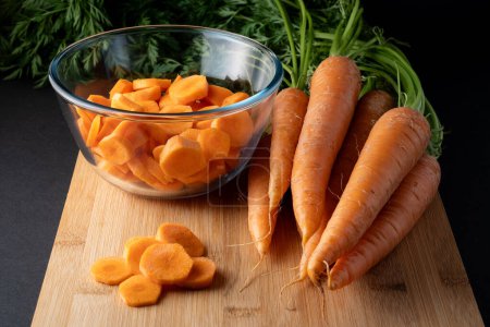 sliced carrots in a round glass bowl and whole carrots on the table