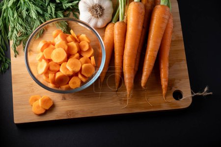 zanahorias en rodajas en un recipiente de vidrio redondo y zanahorias enteras en la mesa