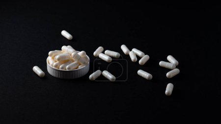 white pills medicine supplement on black background glass of water