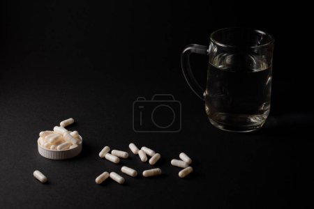 píldoras blancas suplemento de la medicina sobre fondo negro vaso de agua