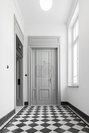 Treppe im klassischen Stil. Stahlgeländer mit Holzelementen. Große graue Haustür zur Wohnung. Geräumiger Flur mit Aufzug