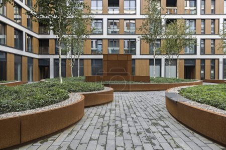 Téléchargez les photos : Bâtiments résidentiels dans une ville européenne. Des blocs modernes d'appartements. Cour avec végétation et éclairage. Finition métal rouille, corten. Garage souterrain - en image libre de droit