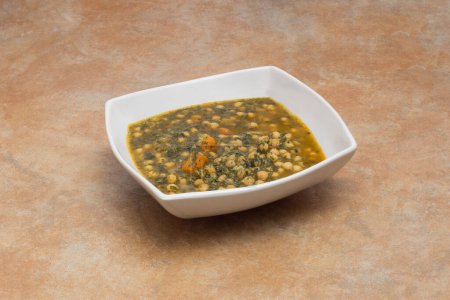 Photo for An elegant deep geometric white ceramic dish with a stew of chickpeas with spinach on a natural stone countertop - Royalty Free Image