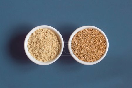 Foto de Top view of a close-up of two ceramic bowls side by side with whole and powdered flax seeds. Superfood. - Imagen libre de derechos