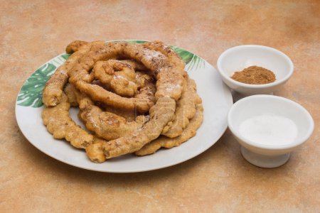Photo for A plate of fried dough twists with two small bowls of powdered sweetener and cinnamon powder on the side.  Food, desserts, and snacks. - Royalty Free Image