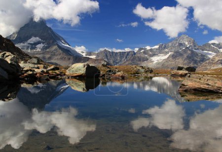 Photo for A landscape with a smooth Riffelsee lake surface and mountains and clouds reflected in it, on a mountain Gornergrat, near Zermatt, in southern Switzerland - Royalty Free Image