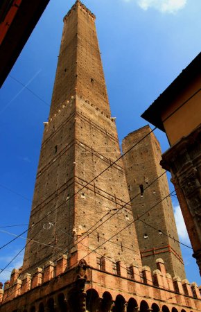 Photo de deux tours médiévales Asinelli et Garisenda, photographiées d'un angle contre un ciel bleu avec des nuages dans le centre historique de Bologne, Italie