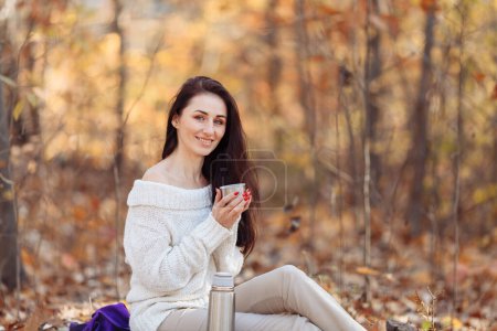 Foto de Hermosa joven estudiante ucraniana sentada al aire libre con una taza en las manos, feliz mujer atractiva de Oriente Medio posando fuera de una calle de la ciudad, llevando una mochila y sonriendo a la cámara detrás - Imagen libre de derechos