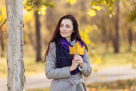 Foto de Una hermosa chica con el pelo oscuro, un abrigo húmedo y una bufanda púrpura sostiene una carta. fondo borroso y hojas borrosas visibles arriba - Imagen libre de derechos
