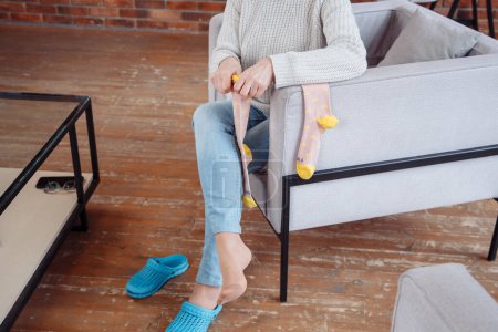 Foto de Una mujer sentada en el suelo y poniéndose calcetines blancos y acogedores de algodón en los pies, calentando las piernas y el cuerpo en otoño e invierno. Foto de alta calidad - Imagen libre de derechos