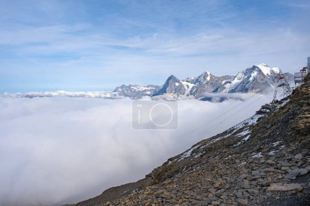 View of Swiss Alps over clouds on a bright sunny day from Schilthorn summit in Switzerland. Cable car pylon