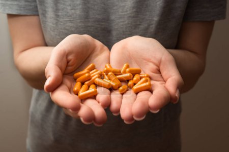 Foto de Las manos de la mujer sostienen un puñado de píldoras de cúrcuma naranja, suplementos saludables, concepto de bienestar, enfoque selectivo tiro de cerca - Imagen libre de derechos