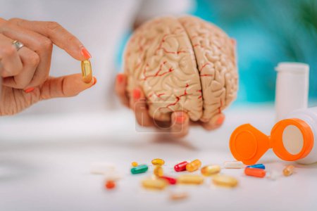 Cognitive improvement or brain supplements. Woman holding a supplement capsule and a model brain.