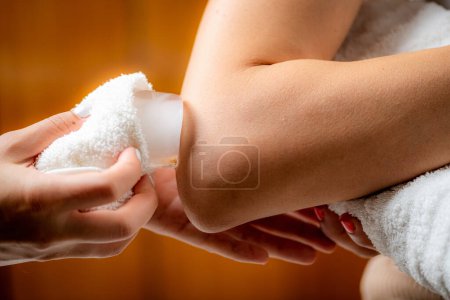 Téléchargez les photos : Massage sur glace par cryothérapie du coude. Mains d'un thérapeute plaçant de la glace directement sur une épaule douloureuse pour soulager la douleur, réduire l'inflammation et le gonflement et favoriser la guérison. - en image libre de droit
