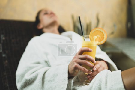 Photo for Woman in Bathrobe Lying on Tepidarium Bed and Drinking Lemonade. - Royalty Free Image
