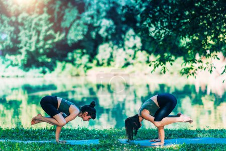 Téléchargez les photos : Femmes faisant du yoga au bord de l'eau. Crane- Corbeau bras debout - en image libre de droit