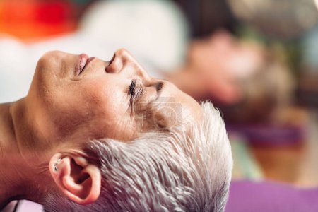 Foto de Terapia de meditación guiada. Mujer mayor meditando, acostada en el suelo - Imagen libre de derechos