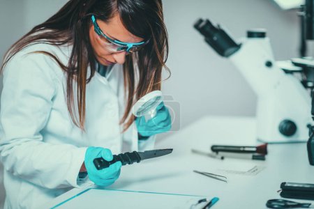 Photo for Forensic Science in Lab. Forensic Scientist examining knife with blood evidences - Royalty Free Image