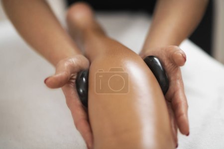 Photo for Stone massage calf spasm treatment with black basalt stones - Royalty Free Image