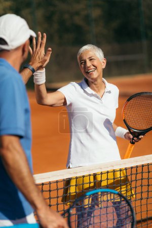 Téléchargez les photos : Entraîneur de tennis Pratiquant le service avec la femme aînée sur la classe de tennis extérieure. Donner haut cinq. - en image libre de droit