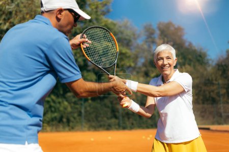 Foto de Entrenamiento de mujeres mayores con instructor de tenis en una cancha de arcilla - Imagen libre de derechos