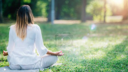 Photo for Meditating by the water, young woman in white, green nature background - Royalty Free Image
