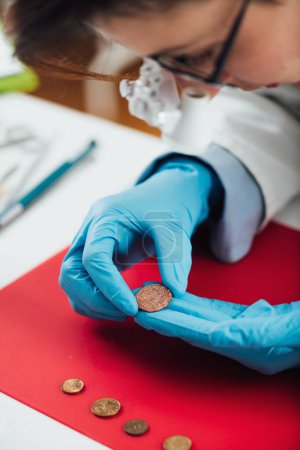 Photo for Numismatics expert examines a collection of coins, using magnifying goggles - Royalty Free Image