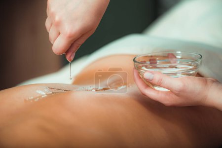 Téléchargez les photos : Huile de massage. Thérapeute verser de l'huile de massage aromatique sur les femmes dos - en image libre de droit